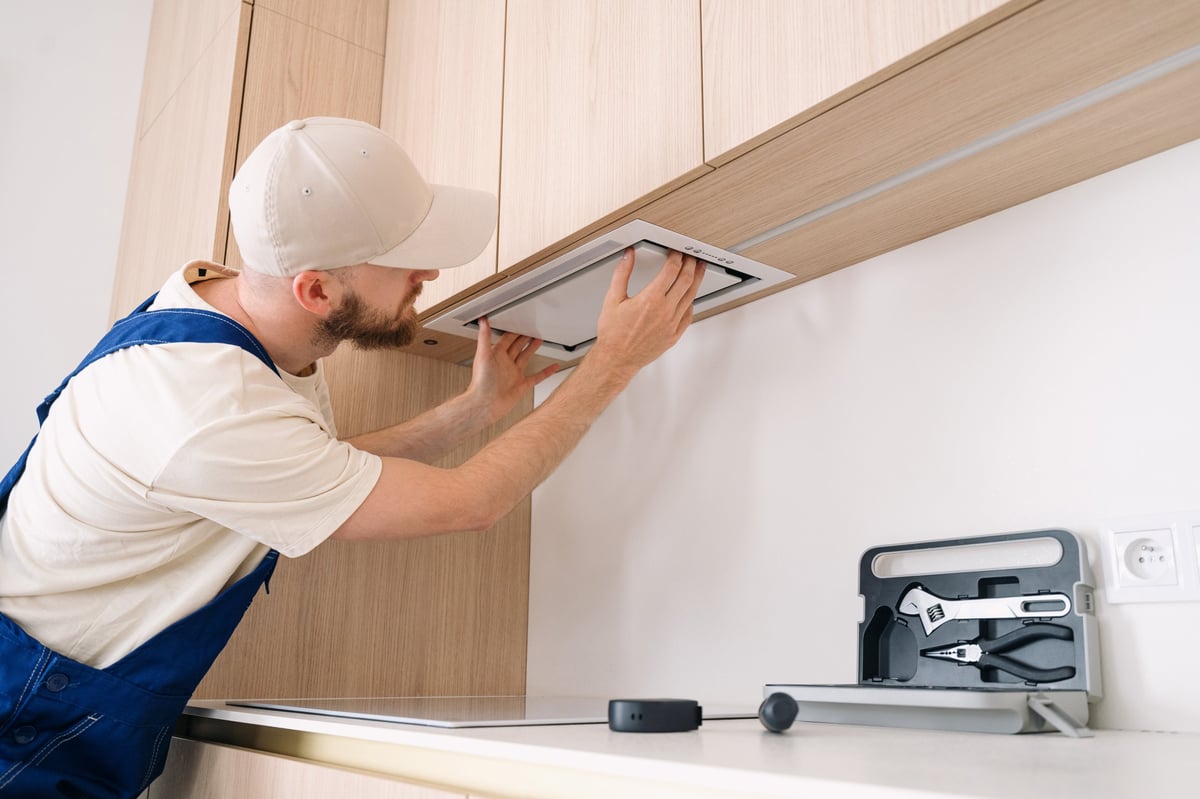 Professional technician installing range hood in apartment unit