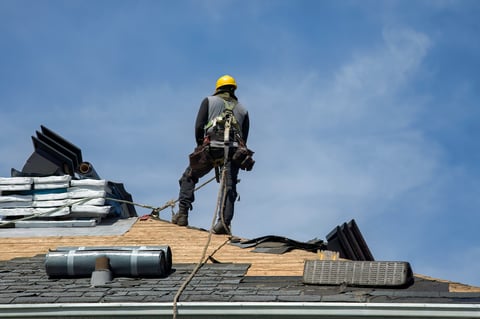 Construction worker using pneumatic nailer and safety helmet applying roofing materials