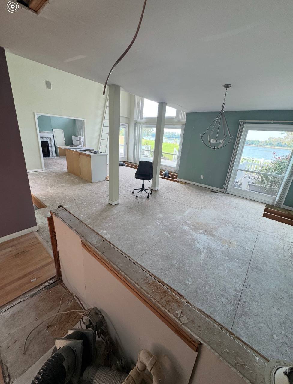 Unfinished modern office or apartment space with concrete flooring, large windows, teal accent wall, pendant light, and wooden trim visible from elevated view