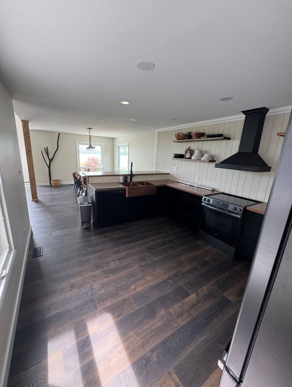 Modern open-concept kitchen with black island, dark wood flooring, stainless steel appliances, and white shiplap backsplash