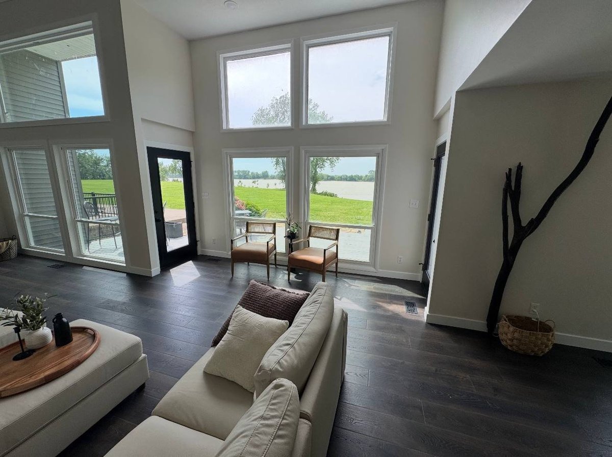 Modern living room with cream sofa, dark hardwood floors, and large windows overlooking green outdoor landscape